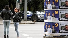 Unas mujeres esperan para cruzar la carretera cerca de los carteles de la campaña electoral en Sofía, Bulgaria, el sábado 1 de octubre de 2022.