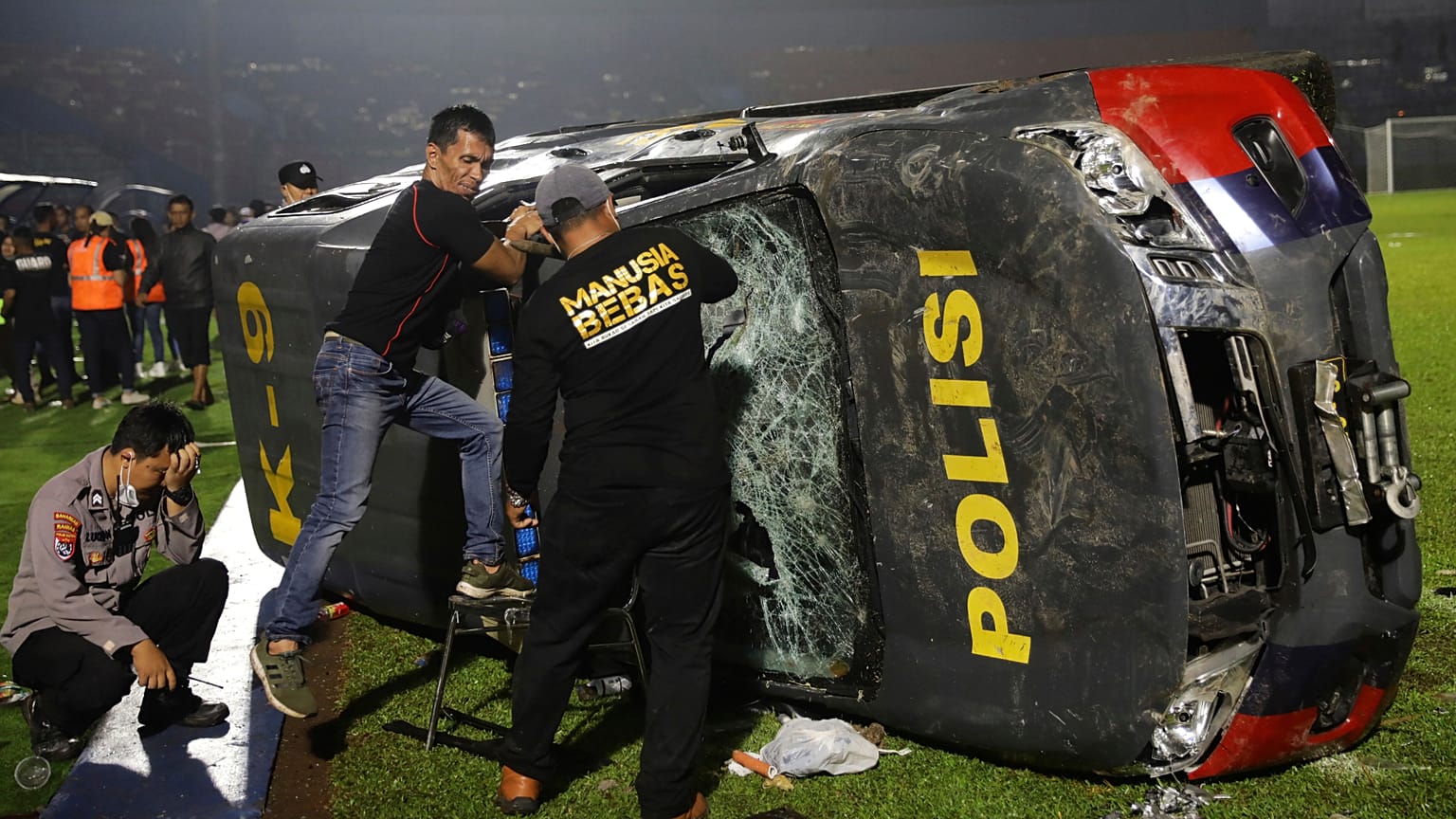 Agentes da polícia avaliam os danos numa viatura das autoridades tombada no relvado