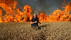 A journalist runs from a burning wheat field during his assignment after Russian shelling, a few kilometres from Ukrainian-Russian border in the Kharkiv region, July 29, 2022.
