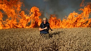 A journalist runs from a burning wheat field during his assignment after Russian shelling, a few kilometres from Ukrainian-Russian border in the Kharkiv region, July 29, 2022.