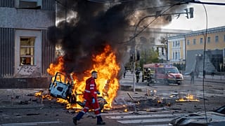 Un travailleur médical marche à côté d'une voiture qui brûle suite aux attaques à Kyiv, le 10 octobre 2022.