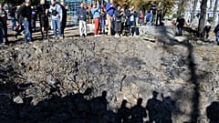 People stand by a rocket crater next to a child playground in central Kyiv on October 10, 2022 after Ukraine's capital was hit by multiple Russian strikes.