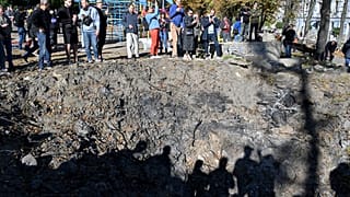 People stand by a rocket crater next to a child playground in central Kyiv on October 10, 2022 after Ukraine's capital was hit by multiple Russian strikes.