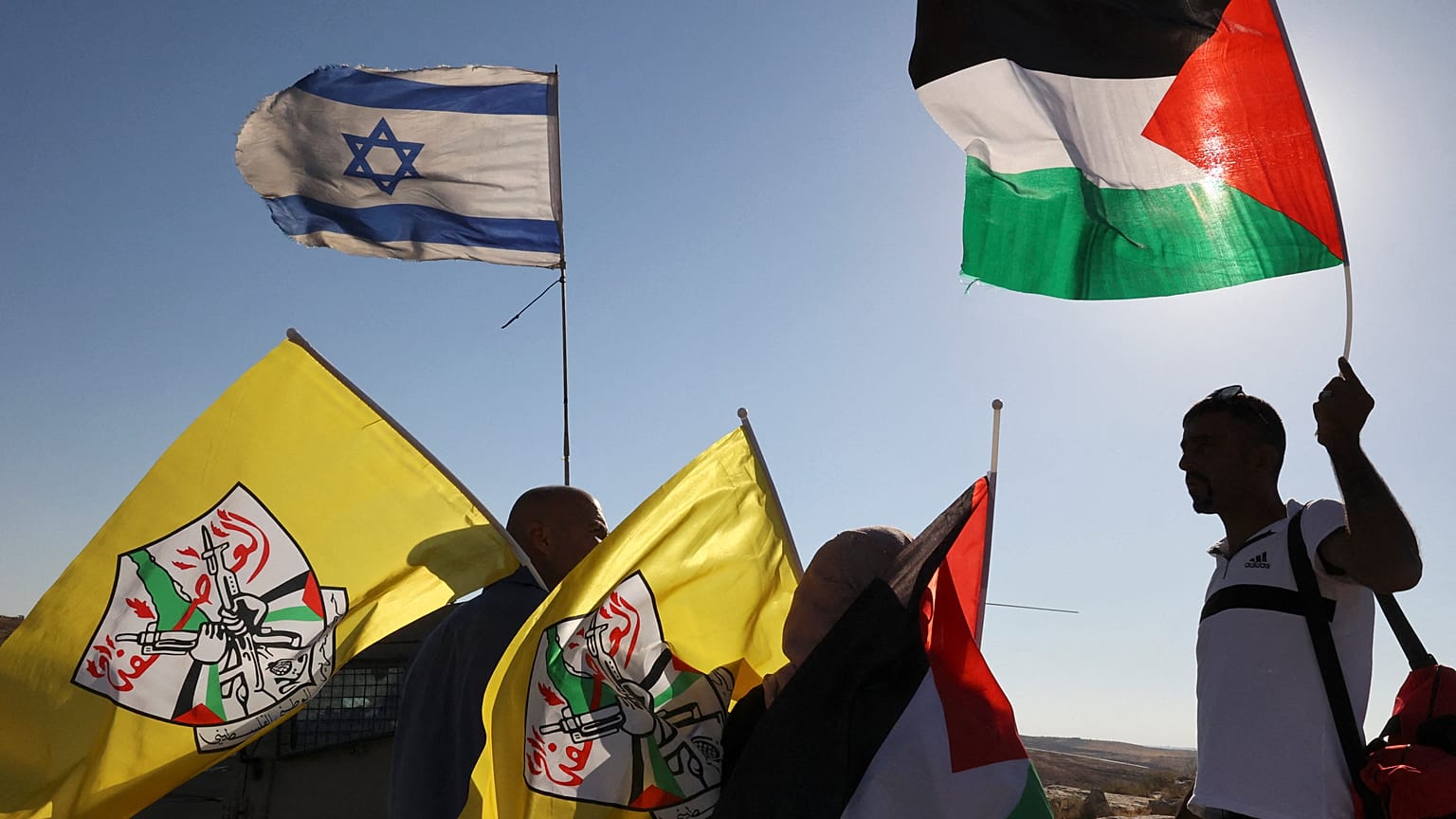فلسطينيون يرفعون علمهم الوطني وعلم فتح وهم يقفون بالقرب من جنود إسرائيليين يؤمنون مسيرة للمستوطنين الإسرائيليين، بالقرب من الخليل بالضفة الغربية المحتلة، في 21 يونيو 2021