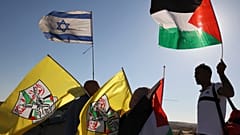 فلسطينيون يرفعون علمهم الوطني وعلم فتح وهم يقفون بالقرب من جنود إسرائيليين يؤمنون مسيرة للمستوطنين الإسرائيليين، بالقرب من الخليل بالضفة الغربية المحتلة، في 21 يونيو 2021