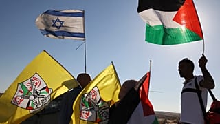 فلسطينيون يرفعون علمهم الوطني وعلم فتح وهم يقفون بالقرب من جنود إسرائيليين يؤمنون مسيرة للمستوطنين الإسرائيليين، بالقرب من الخليل بالضفة الغربية المحتلة، في 21 يونيو 2021