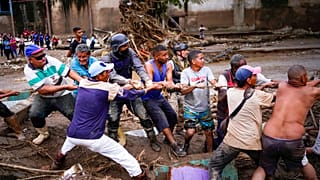 Local residents and relief workers pull a rope to remove wreckage in search for survivors from a home destroyed by flooding.