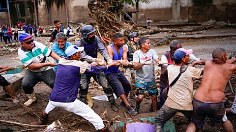 Local residents and relief workers pull a rope to remove wreckage in search for survivors from a home destroyed by flooding.