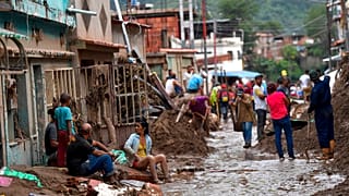 Residentes locales descansan mientras sus vecinos limpian el barro y recuperan sus pertenencias en una calle inundada mientras el sol se pone en Las Tejerías, Venezuela