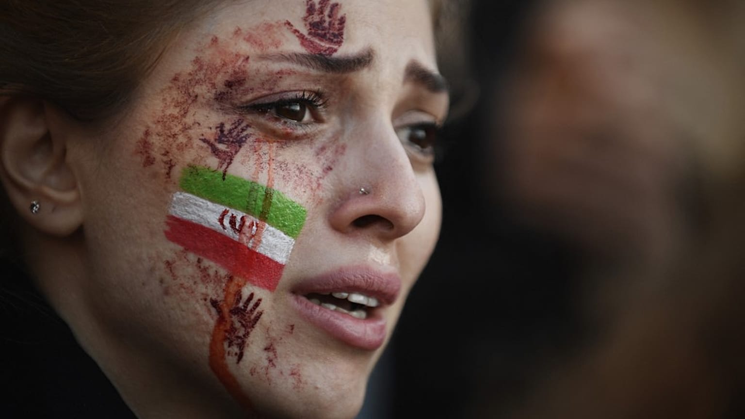 A demonstrator with an Iranian flag and red hands painted on her face attends a rally in support of Iranian protests, in Paris on October 9, 2022.