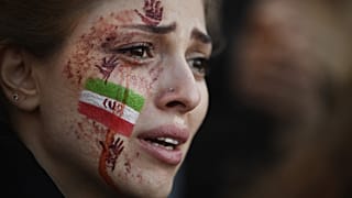 A demonstrator with an Iranian flag and red hands painted on her face attends a rally in support of Iranian protests, in Paris on October 9, 2022.