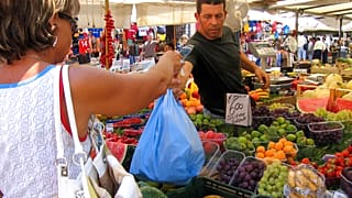 in questa immagine d'archivio, una donna paga per la spesa in un chiosco di frutta e verdura in un mercato di Roma, venerdì 30 luglio 2004