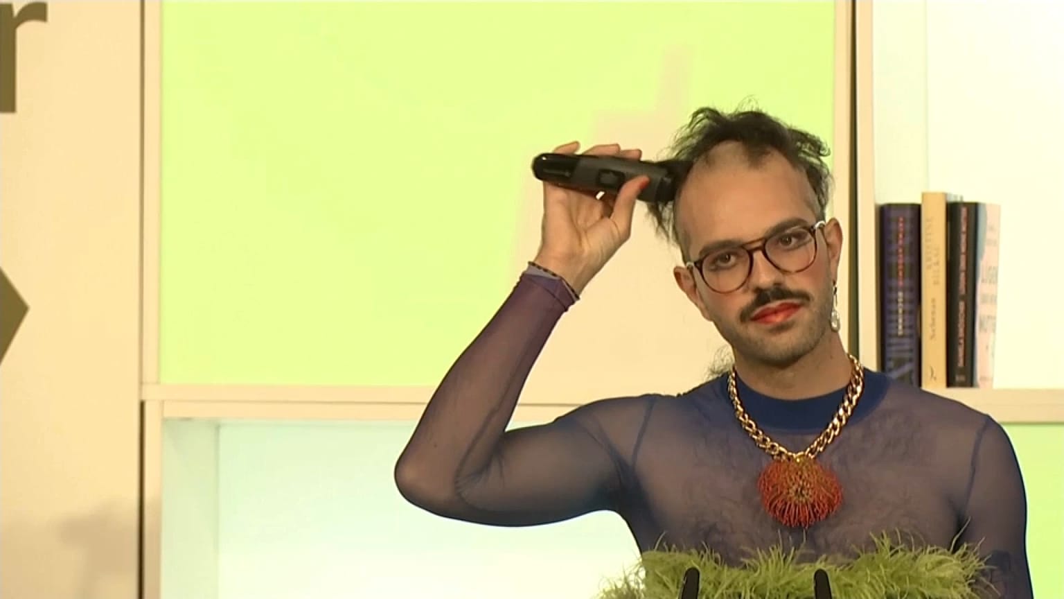 Kim de l'Horizon rasiert sich am Rednerpult die Haare.
