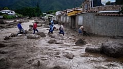 Personas vadean una carretera llena de barro tras el desbordamiento de un río provocado por las fuertes lluvias en El Castaño, Venezuela