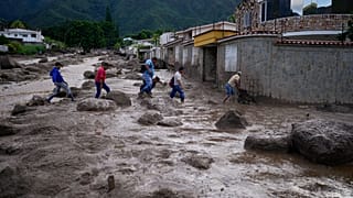 Personas vadean una carretera llena de barro tras el desbordamiento de un río provocado por las fuertes lluvias en El Castaño, Venezuela