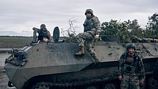 Ukrainian servicemen and a servicewoman, centre, pose for a photo with their armoured vehicle near Bakhmut, 22 October 2022