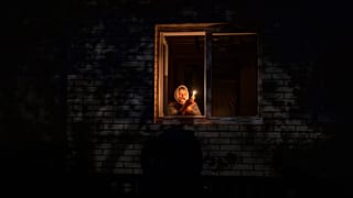Catherine, 70, looks out the window while holding a candle for light inside her house during a power outage, in Borodyanka, Kyiv region