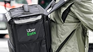 An Uber Eats delivery person rides a bicycle through a commercial district