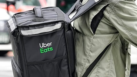 An Uber Eats delivery person rides a bicycle through a commercial district in Tokyo, Japan Tuesday, Aug. 30, 2022.(AP Photo/Shuji Kajiyama)