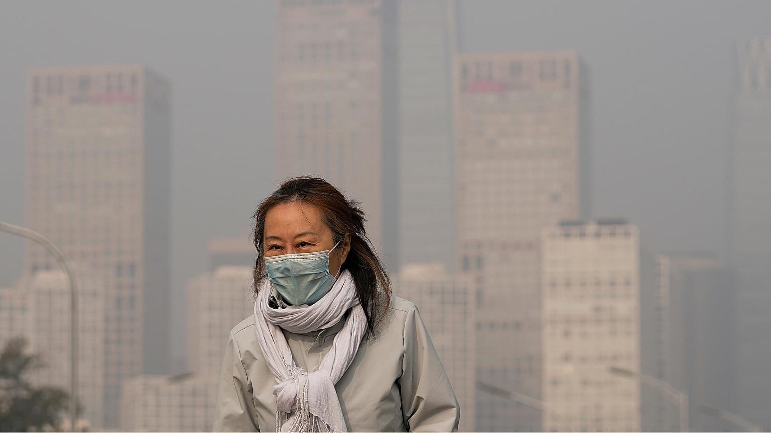 A woman wearing a face mask walks against the office buildings in Central Business District shrouded by pollution haze in Beijing.