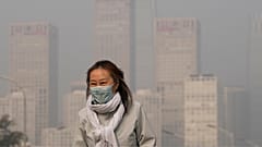 A woman wearing a face mask walks against the office buildings in Central Business District shrouded by pollution haze in Beijing.