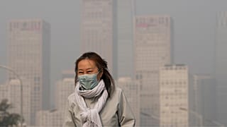 A woman wearing a face mask walks against the office buildings in Central Business District shrouded by pollution haze in Beijing.