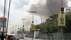 Uma coluna de fumo eleva-se sobre a cidade enquanto as pessoas descem uma rua após uma grande explosão perto do Ministério da Educação, em Mogadíscio, a 29 de outubro de 2022
