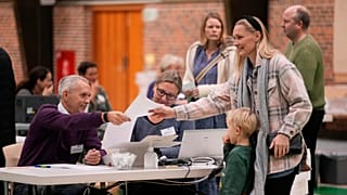 Eleitora acompanhada de uma criança recebe o boletim de voto em Vaerloese, Dinamarca