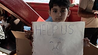 Un enfant migrant tient une pancarte à bord du navire Ocean Viking naviguant dans le détroit de Sicile, en mer Méditerranée, le 2 novembre 2022.