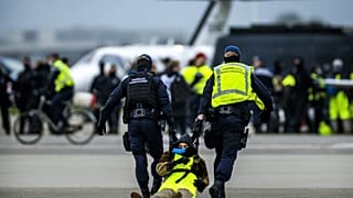 Sicherheitskräfte nehmen einen Klimaaktivisten am Flughafen Schiphol in Amsterdam fest.