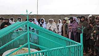 Taliban tarafından yayınlanan fotoğraflarda üst düzey isimlerin yeşil demir parmaklıklarla çevrili basit beyaz bir mezar etrafında toplandığı görülüyor