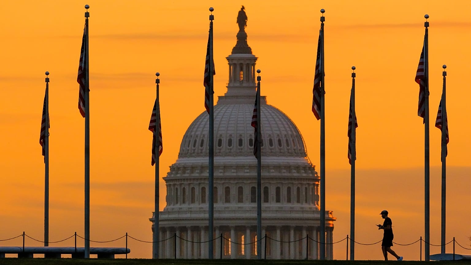 An early morning pedestrian is silhouetted against sunrise as he walks through the U.S. Flags on the National Mall and past the US Capitol Building in Washington