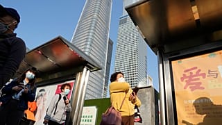 سيدات ينتظرن الحافلة في منطقة الأعمال المركزية في بكين، الصين.