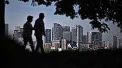 Walkers stroll in Greenwich Park with London's secondary central business district of Canary Wharf seen behind in the spring sunshine on May 6, 2022. 