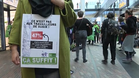 Woman with a sign saying "it is not for the workers to suffer" during protest in a Brussels shopping centre. 
