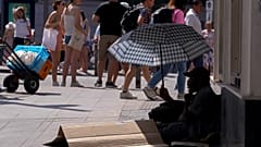 A man sits under an umbrella to shelter himself from the sun while begging for money in the street during hot weather in Madrid, Spain, Saturday, July 16, 2022.