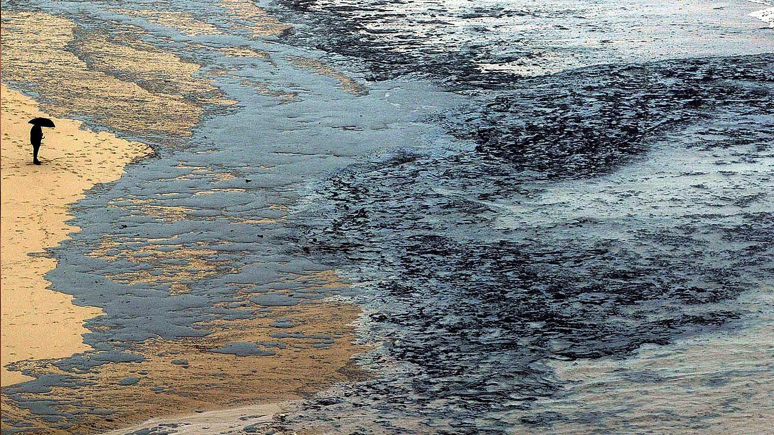 A person looks at oil sludge on a beach in Finisterre in Galicia, 1 December 2003