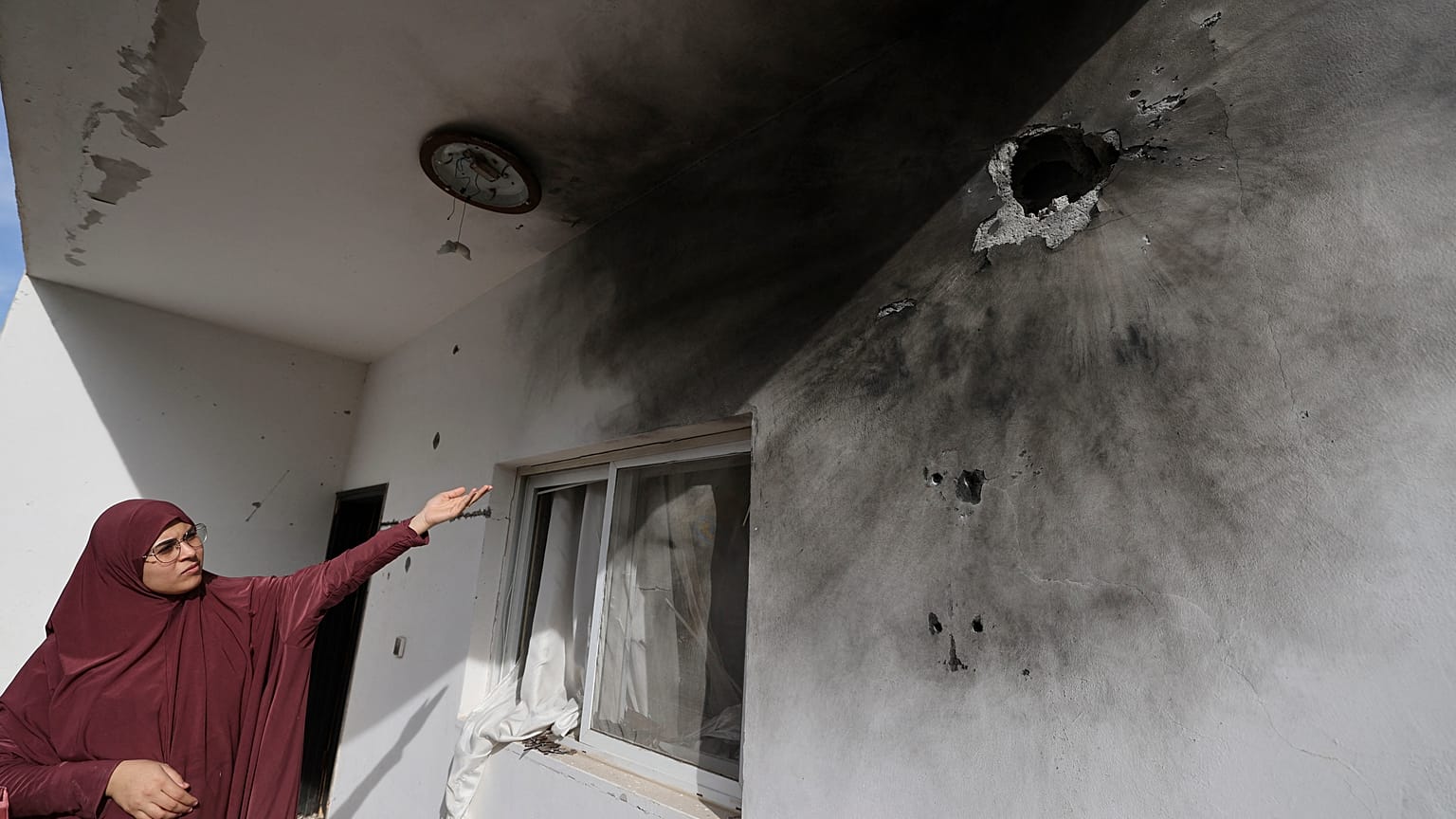 امرأة فلسطينية تشير إلى ثقوب على جدار ناجمة عن اقتحام الجيش الإسرائيلي للمنزل 