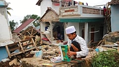 Uma criança apanha livros e manuais escolares nos escombros de uma escola destruída pelo sismo na Indonésia