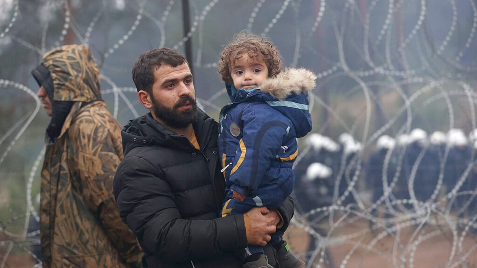 A migrant with a child walks along the barbed wire fence as other gather at the Belarus-Poland border near Grodno, Belarus, Sunday, Nov. 14, 2021.