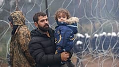 A migrant with a child walks along the barbed wire fence as other gather at the Belarus-Poland border near Grodno, Belarus, Sunday, Nov. 14, 2021.