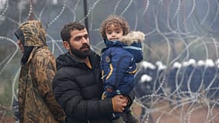 A migrant with a child walks along the barbed wire fence as other gather at the Belarus-Poland border near Grodno, Belarus, Sunday, Nov. 14, 2021.
