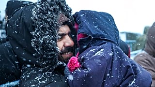 Ein Vater hält sein Kind, während er bei Schneefall vor einem Logistikzentrum am Kontrollpunkt "Kuznitsa" an der belarussisch-polnischen Grenze in der Nähe von Grodno, Belarus