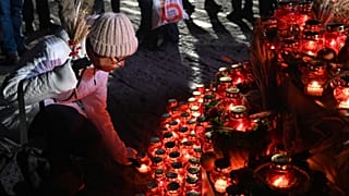 A woman lays symbolic sheave of wheat and lights candle during a commemoration ceremony at a monument to victims of the Holodomor famine