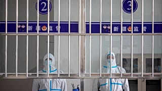 Vegyvédelmi ruhába öltözött covid-ellenőrök Ürümcsiben