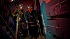 Eine Seniorin wird von Freiwilligen aus ihrem Haus in Cherson geleitet