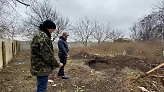 Serguei and Sasha point to the remains of a grave discovered in the village of Pravdyne last week