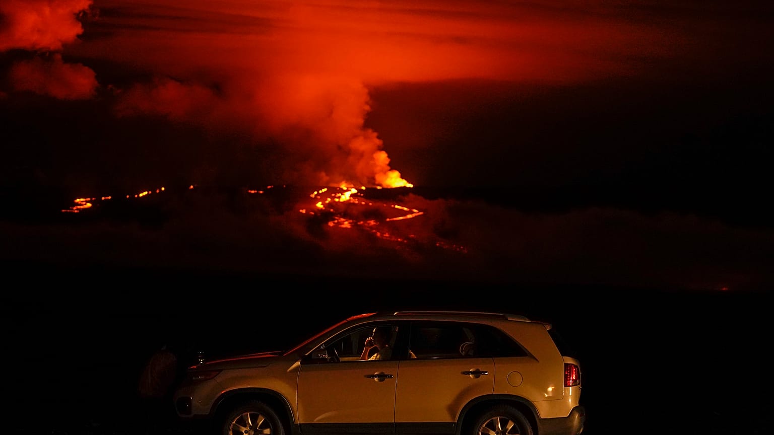 Un hombre habla por teléfono en su coche junto a Saddle Road mientras el volcán Mauna Loa entra en erupción el miércoles 30 de noviembre de 2022, cerca de Hilo, Hawái.