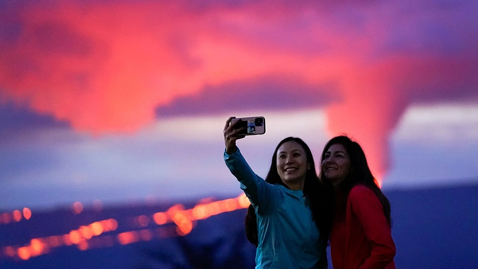 Ingrid Yang, left, and Kelly Bruno, both of San Diego, take a photo in front of lava erupting from Hawaii's Mauna Loa volcano on Wednesday, 30 November.