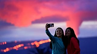 Ingrid Yang, left, and Kelly Bruno, both of San Diego, take a photo in front of lava erupting from Hawaii's Mauna Loa volcano on Wednesday, 30 November.